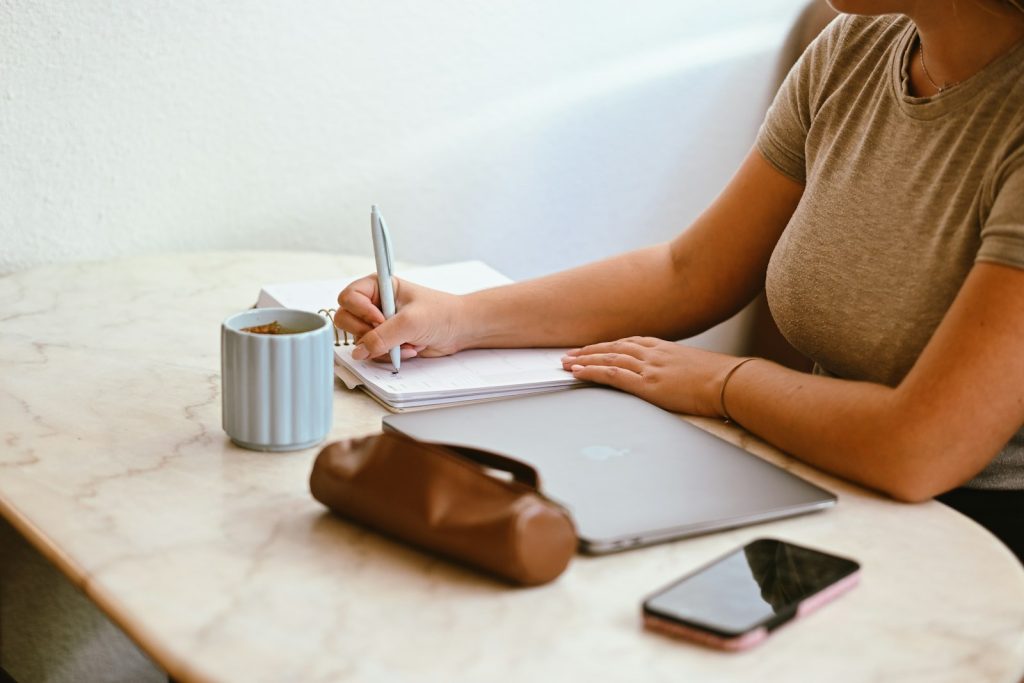 Selbstständig als Copywriter – Texterin schreibt Notizen neben ihrem Laptop