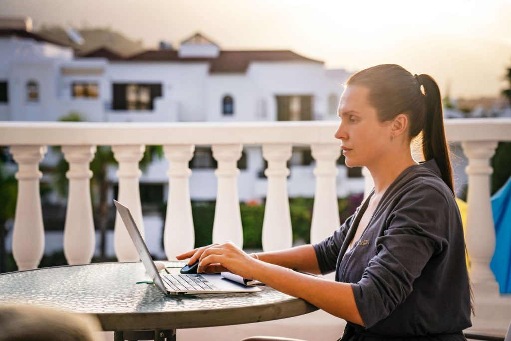 Virtuelle Assistenz von überall – Frau arbeitet am Laptop auf einer sonnigen Terrasse