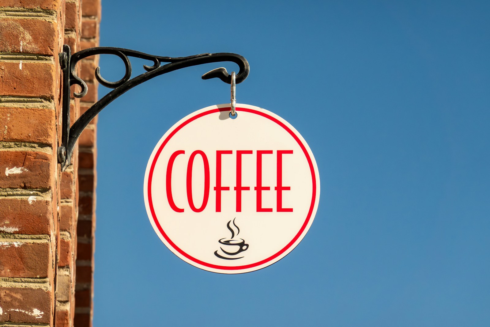 A round coffee sign hangs on a brick wall.