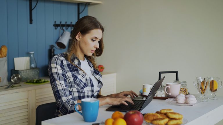 Woman working on laptop in a bright kitchen.