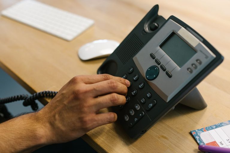 10 gute KI-Telefonassistenten für Unternehmen 2026 (Vergleich) KI-Telefonassistenten für Unternehmen – Hand wählt am Bürotelefon